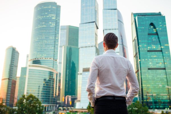 Back view of businessman looking on copy space while standing against glass skyscraper