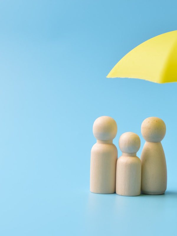 Yellow umbrella and wooden doll figures. Insurance coverage concept.